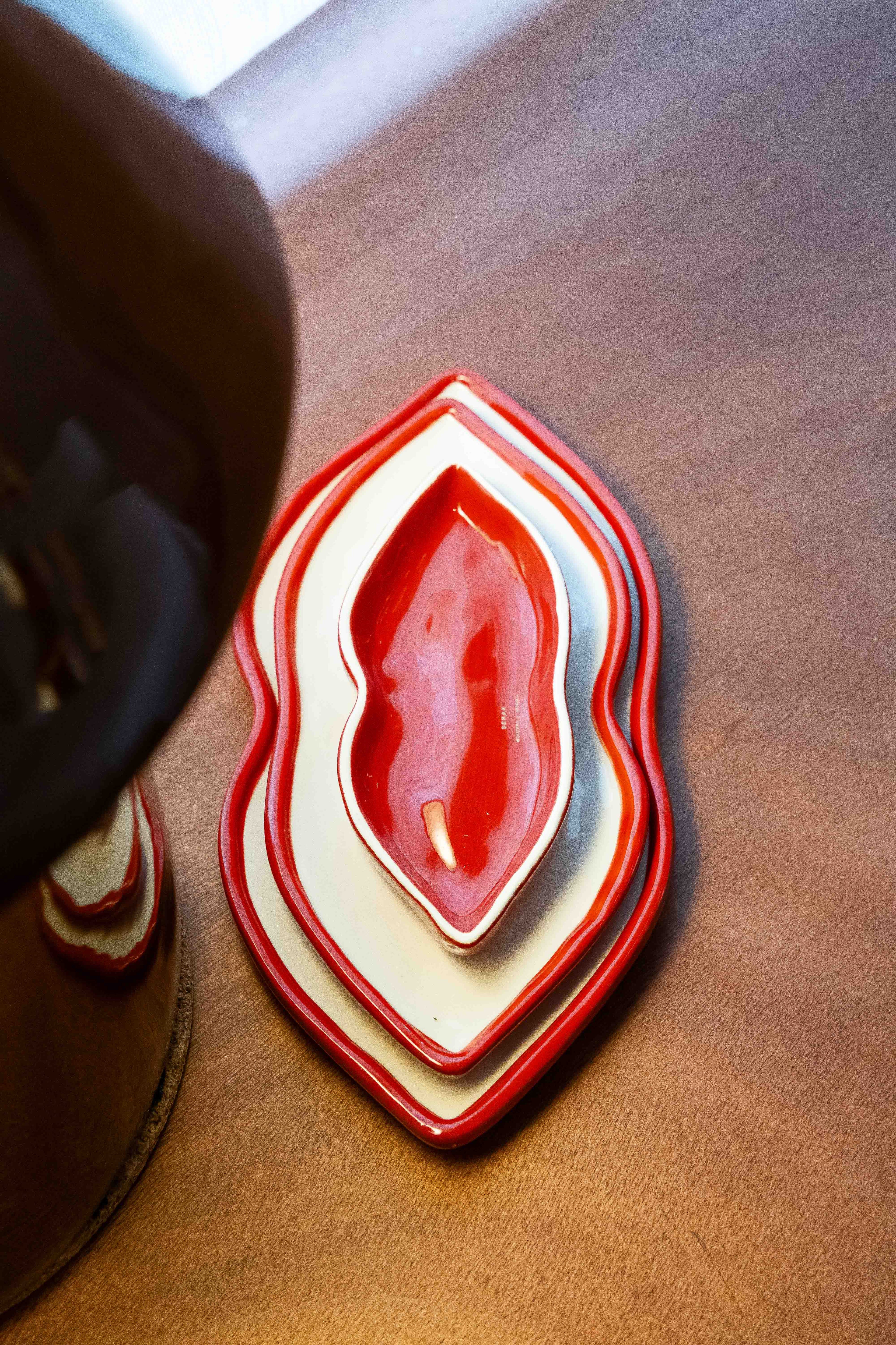 Set of three red and white heart-shaped nesting dishes on a light brown wooden surface.