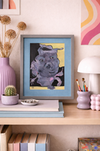 Whimsical abstract animal art painting of a purple creature with multiple eyes, framed in grey with a blue mat, on a shelf.