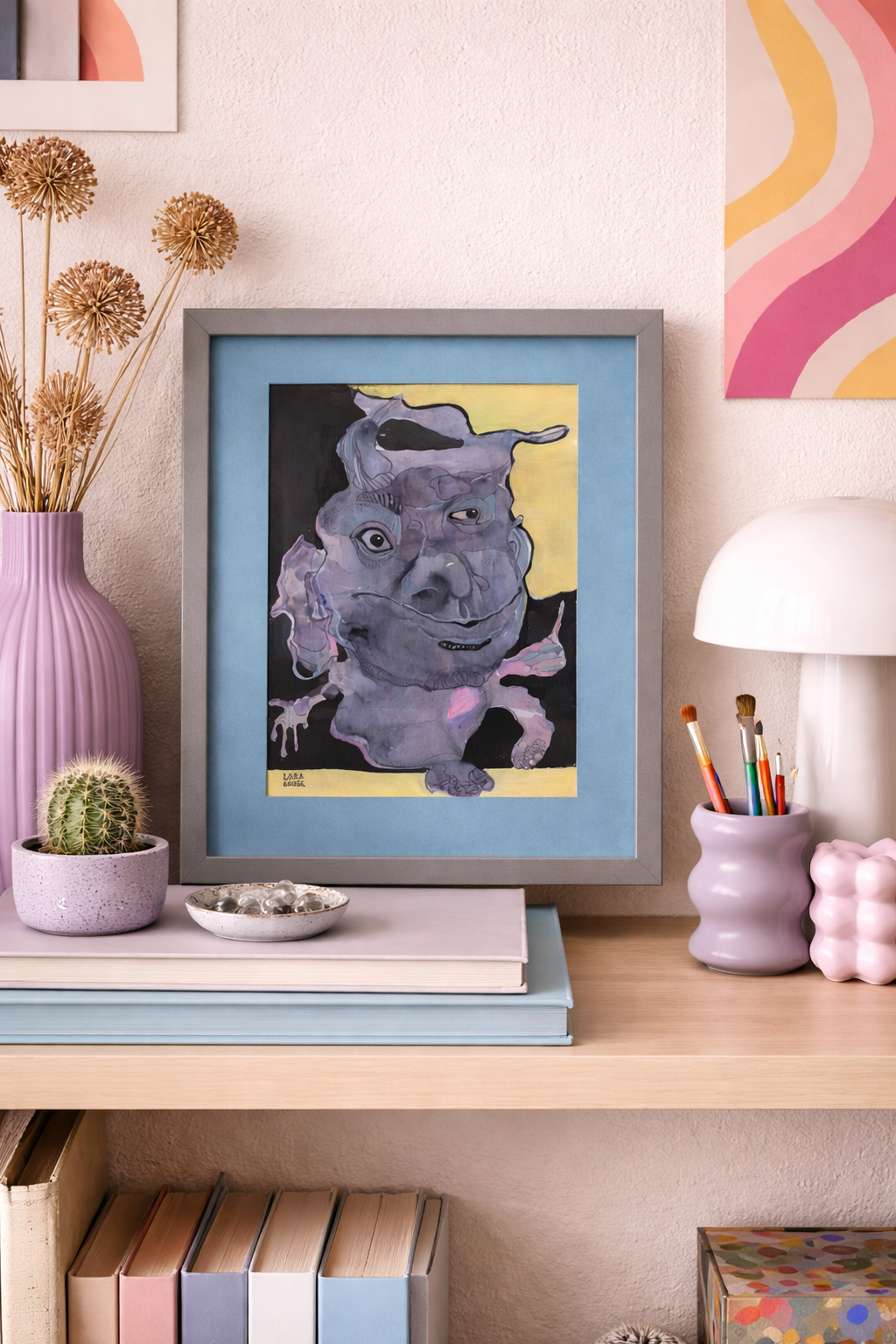 Whimsical abstract animal art painting of a purple creature with multiple eyes, framed in grey with a blue mat, on a shelf.