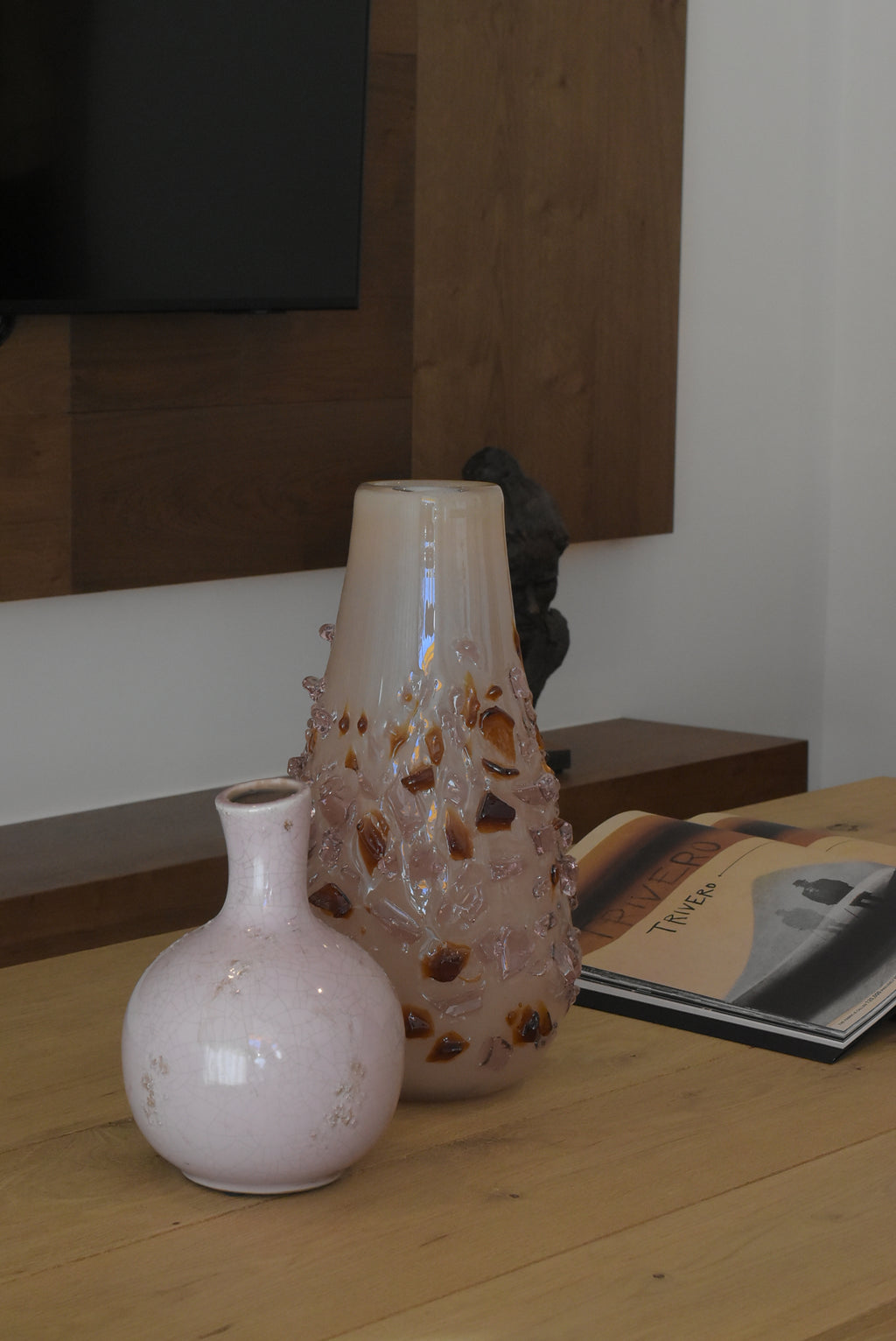 Decorative quartz vase by Object and Story with brown glass embedded in a light pink glass, set on a wood table.