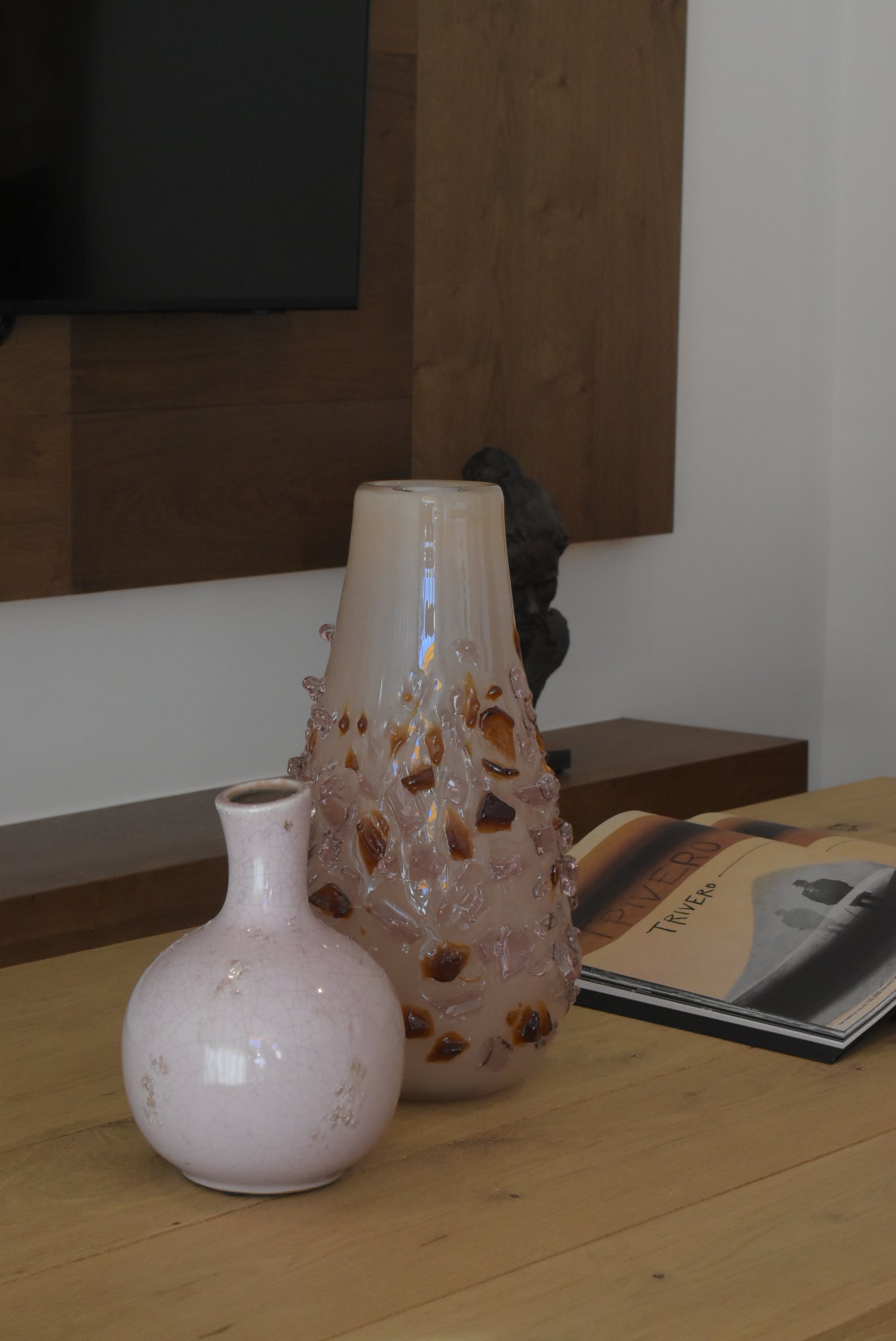 Decorative quartz vase by Object and Story with brown glass embedded in a light pink glass, set on a wood table.