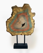 Colorful, gold-accented wood deco piece with concentric rings of teal, orange, and beige, mounted on a black stand.