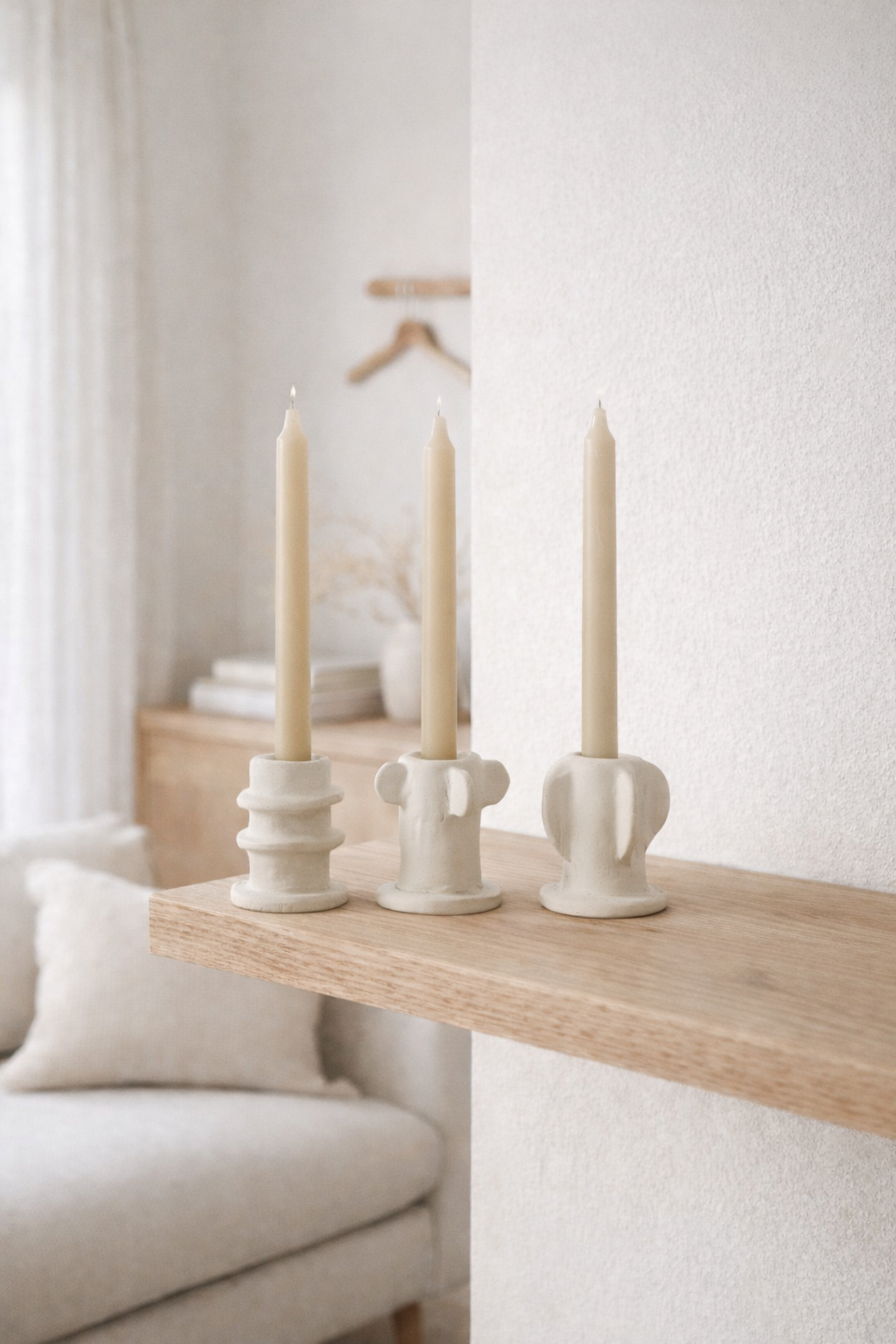 Molly candle holder set with three distinct off-white ceramic candle holders holding beige candles on a wood shelf.