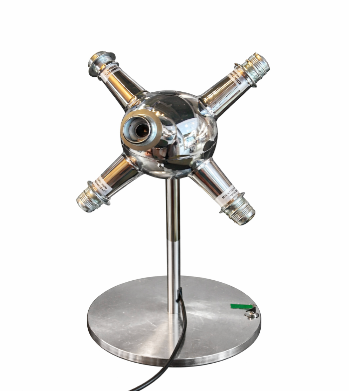 Polished chrome table lamp with a spherical body, central lens, and four radiating arms on a round metal base.