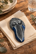 Black, white, and blue painted Pelican Art Stone with intricate abstract lines, resting on folded beige napkins.