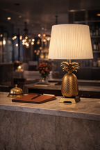 Gold pineapple table lamp with a pleated white shade on a marble counter.