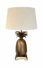 A gold pineapple table lamp with a cream pleated fabric shade and square base.