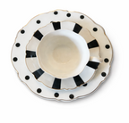 White layered tea cup set with black polka dot plate, striped saucer, and gold trim, overhead view.