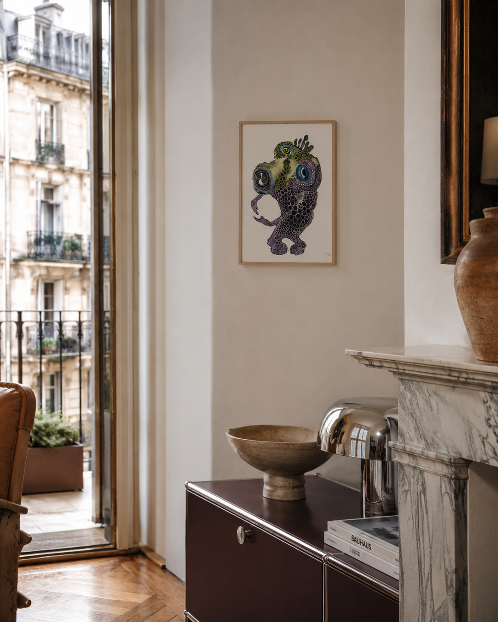 Whimsical framed artwork above modern cabinet in Parisian apartment with marble fireplace and vintage decor