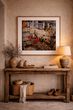 Painting depicting ruins of buildings with red fabrics and a person by Manuel Cohen, framed in wood over a rustic table.