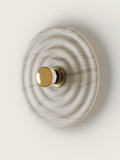 Top-down white marble wall lamp with concentric waves, featuring a gold and clear glass knob on a brass base.