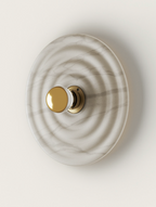 Top-down white marble wall lamp with concentric waves, featuring a gold and clear glass knob on a brass base.