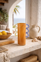 Orange glass vase by Object and Story with blue and yellow wavy handles, styled with lemons and seashells.
