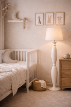 White Alfil floor lamp with a conical shade and elegant sculpted base, in a cozy nursery.