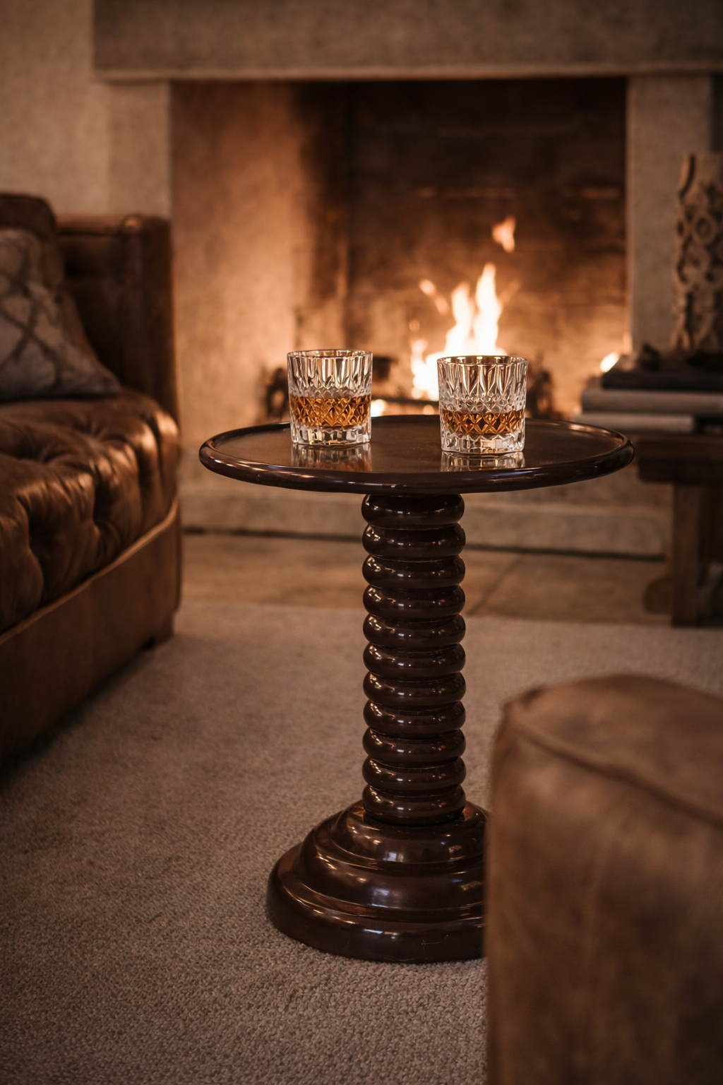 Dark brown polished wood side table with a round top and stacked ring base, holding two whiskey glasses.