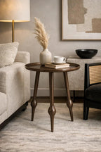 Dark brown round side table with tapered legs featuring bulbous details, styled with a vase, books, and teacup.