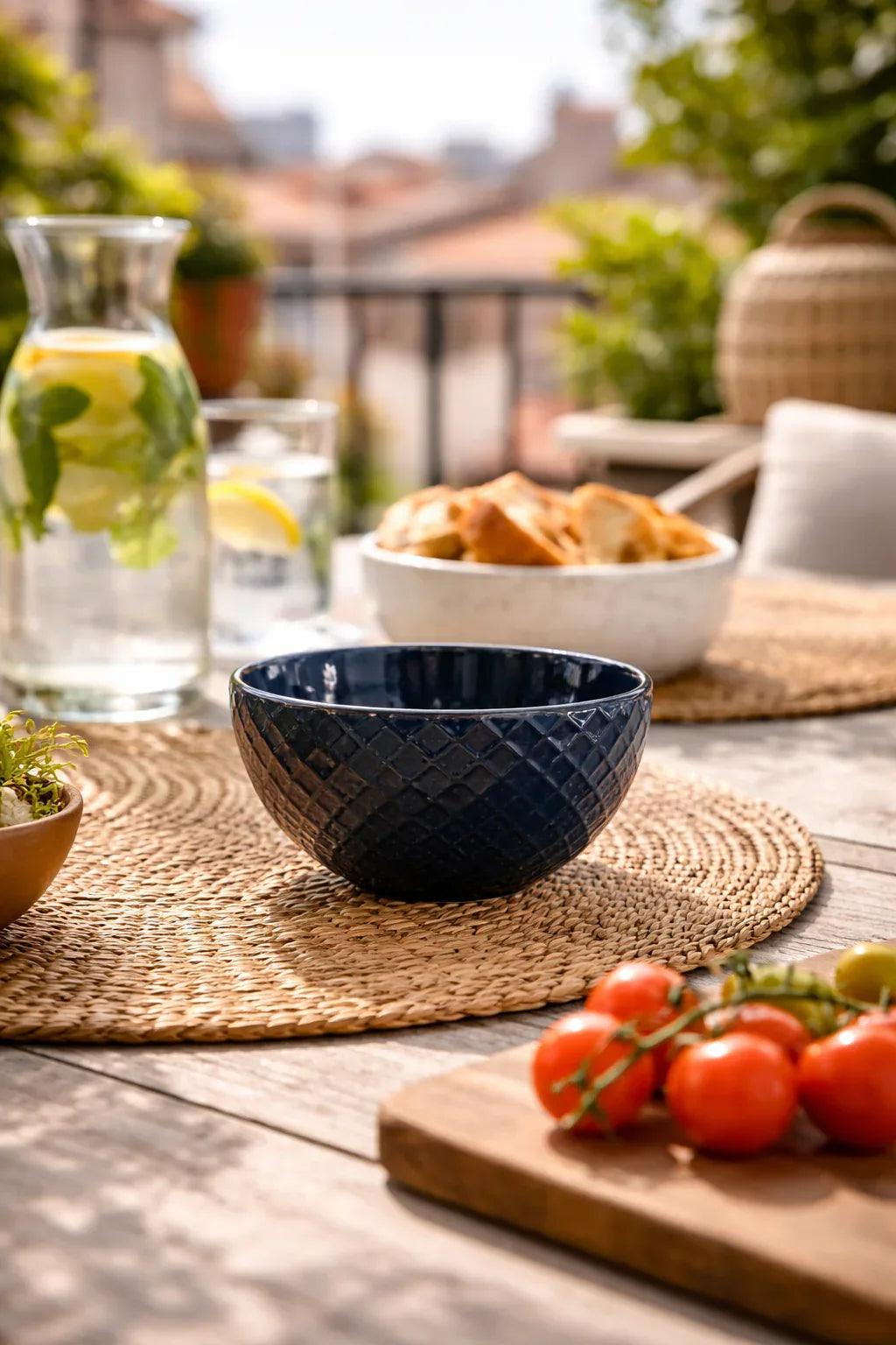 A blue bowl from a set, with a diamond textured pattern, on a woven placemat in an outdoor setting.