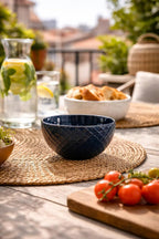 A blue bowl from a set, with a diamond textured pattern, on a woven placemat in an outdoor setting.