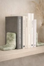 Green marble bookends by Object and Story, holding books on a wooden shelf, with a decorative vase in the background.
