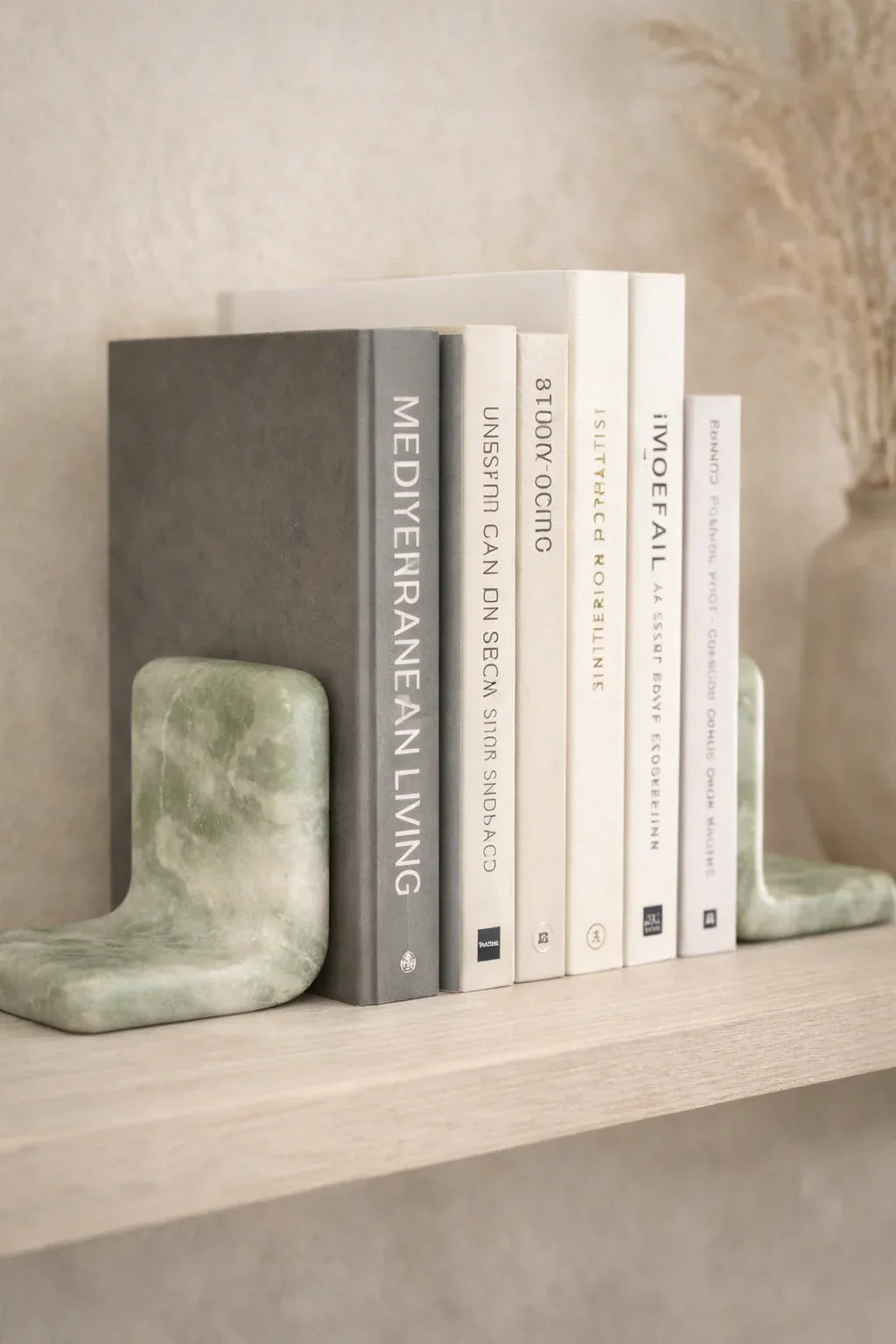 Green marble bookends by Object and Story, holding books on a wooden shelf, with a decorative vase in the background.
