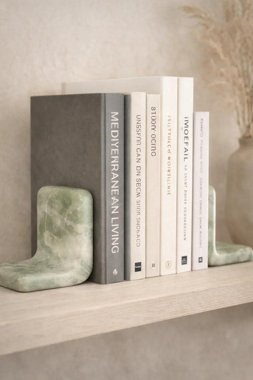 Two green marble L-shaped bookends with natural veining holding books on a light wooden shelf.