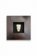Zen Buda image carved in off-white material, displayed in a dark wood shadow box frame against a black background.