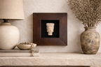 Light-colored Zen Buda carved bust in a dark wood frame displayed on a textured wall above a rustic shelf.