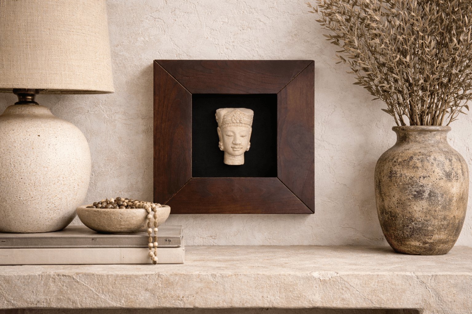 Light-colored Zen Buda carved bust in a dark wood frame displayed on a textured wall above a rustic shelf.