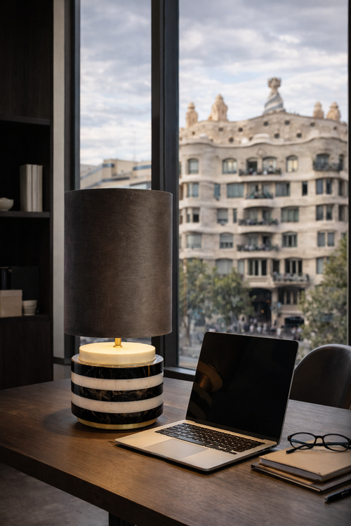 Elegant table lamp with a dark fabric shade and a base of stacked black and white marble rings with brass accents, on a wooden desk.