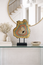 Gold-edged, painted wood slice deco piece on a black stand, displaying concentric rings of teal, orange, and natural wood.