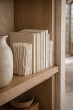 Daria book holder, off-white with a textured, wavy, vertical ridged design, on a light wood shelf.