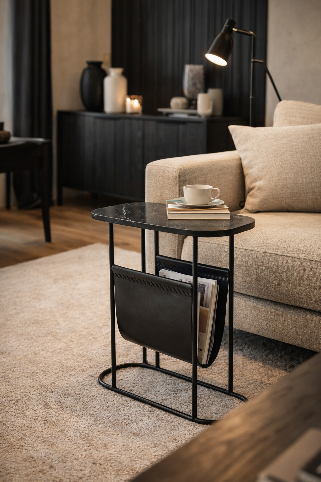 Black marble oval side table with black metal frame and integrated black leather magazine holder, by a sofa.