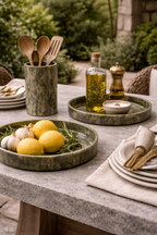 Green, marble-look tray styled with lemons, garlic, and rosemary on a textured grey outdoor table.
