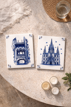 Two white ceramic tiles with blue illustrations of Barcelona architecture, one of an ornate balcony and the other a cathedral.