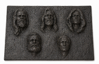 Dark metal wall sculpture with five distinct bas-relief male faces, three above two, with varied beards and long hair.