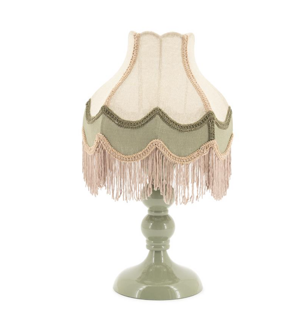 Table lamp with a sage green base and scalloped fabric shade featuring cream, sage green, and light brown fringes.