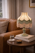 Sage green Fringaloo Table Lamp with a fringed scalloped fabric shade, placed on a wooden side table.