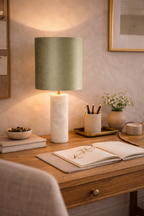 Jade green velvet table lamp with a cylindrical white marble base, casting warm light on a wooden desk.