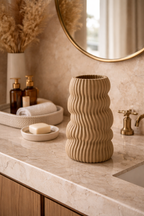 Large sandy beige wavy textured vase on a light marble bathroom counter.