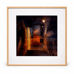Framed painting titled Escala by Manuel Cohen, showing a layered dark urban scene with orange streetlights and a staircase, in a wood frame.