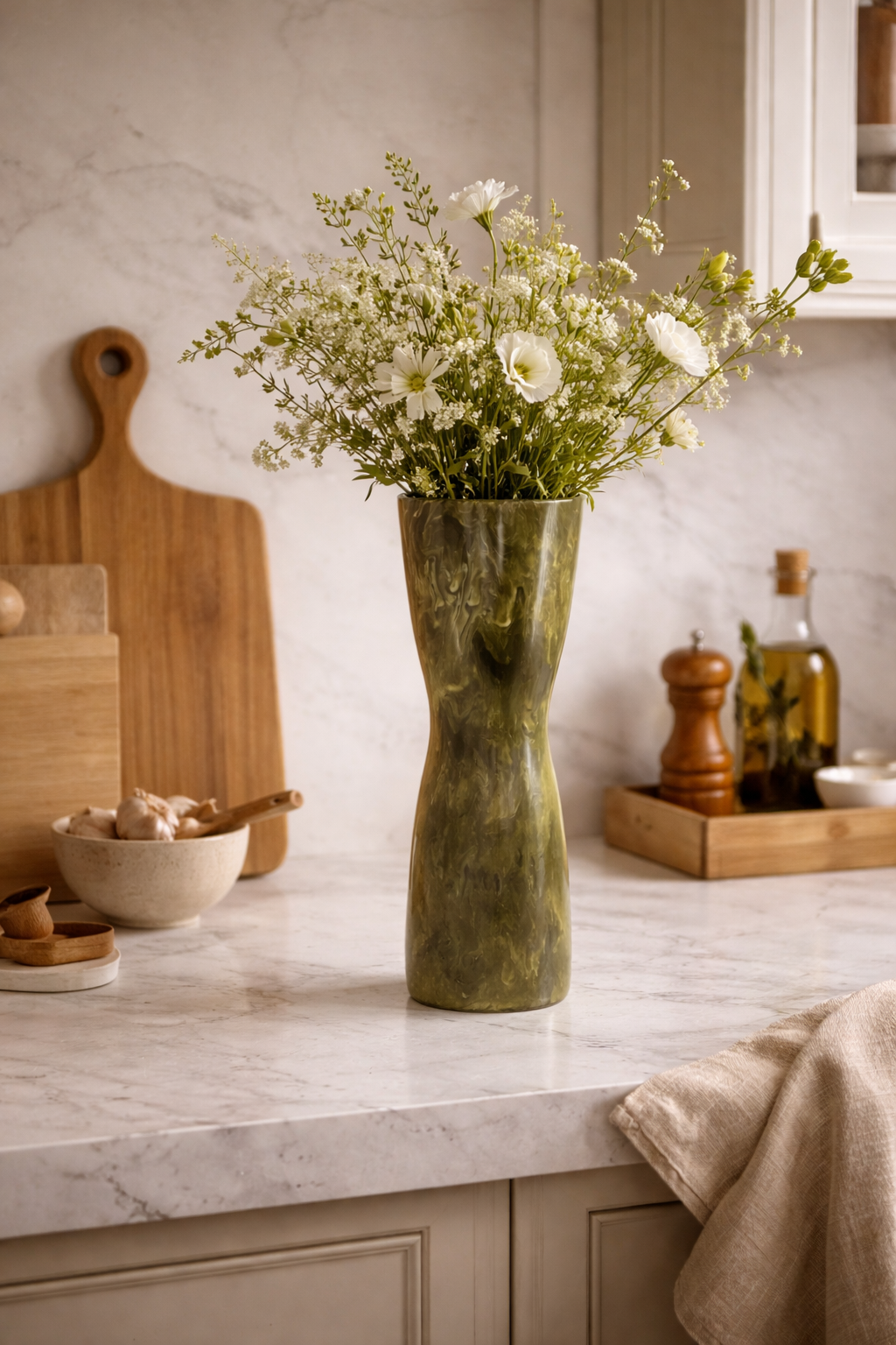 Green marbled vase by Melu with an organic shape and narrow waist, holding white flowers on a kitchen counter.