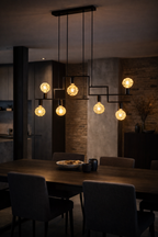 Geometric black metal pendant light with eight warm bulbs, some textured, hanging over a dining table.