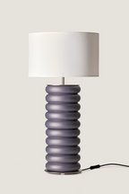Table lamp with a white drum shade and a stacked ribbed matte purple-grey base.