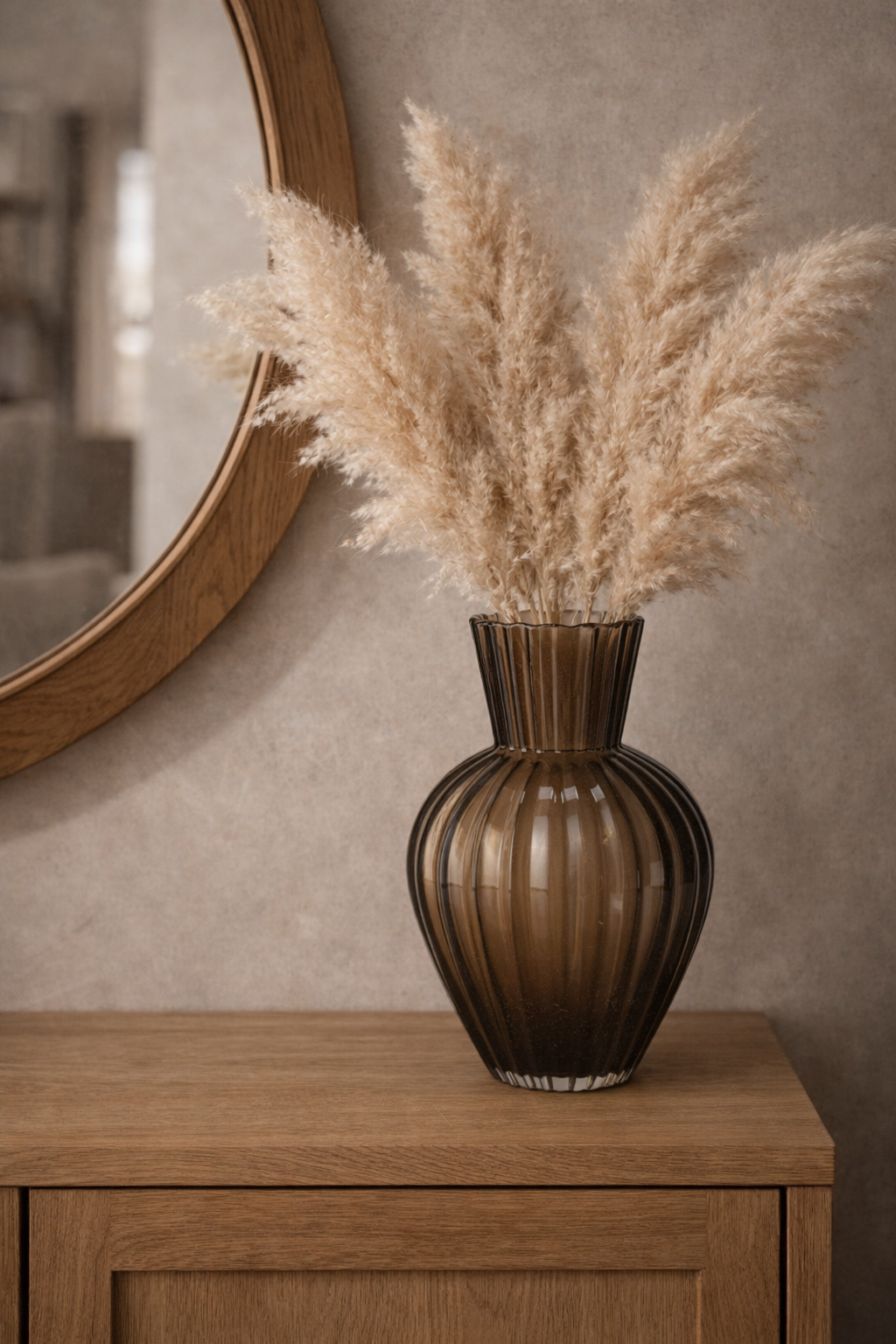 Brown ribbed glass vase holding dried pampas grass, displayed on a wooden cabinet.