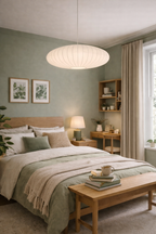 White ribbed oval hanging lamp illuminating a cozy bedroom with sage green walls and wooden furniture.