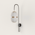 Dark metal wall lamp with an elongated light fabric shade and golden accent band, mounted on a cream wall.