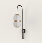 Dark metal wall lamp with an elongated light fabric shade and golden accent band, mounted on a cream wall.
