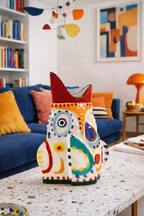 Multicolored ceramic vase with abstract, whimsical patterns and a red pointed rim, on a speckled table.