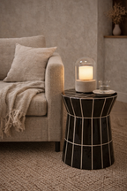 Black tiled side table with white grout lines and a tapered shape, holding a lamp next to a sofa.