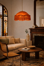 Solara hanging lamp with an orange fringed shade, suspended from a brass rod in a cozy living room.